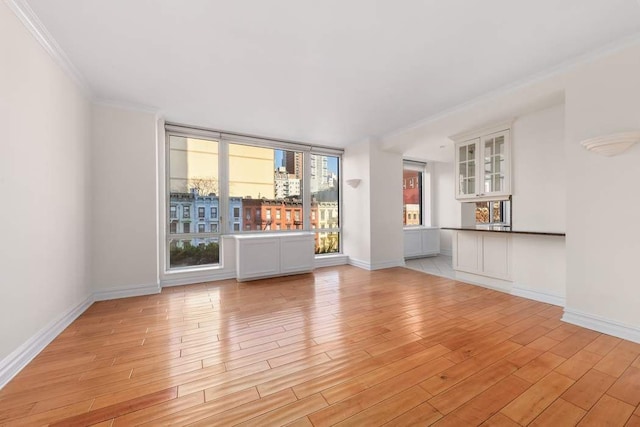 unfurnished living room with crown molding, baseboards, and light wood-type flooring