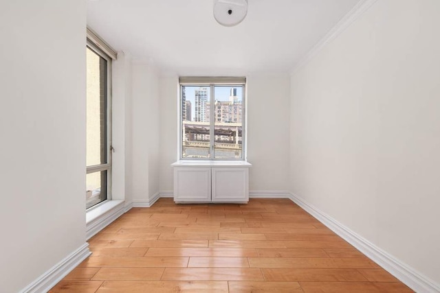 empty room with light wood-style floors, ornamental molding, and baseboards