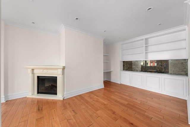 unfurnished living room featuring crown molding, built in shelves, wood finished floors, baseboards, and a glass covered fireplace