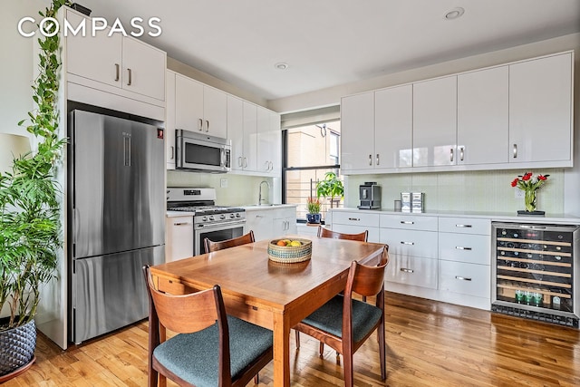 kitchen with appliances with stainless steel finishes, light countertops, beverage cooler, light wood-style flooring, and tasteful backsplash