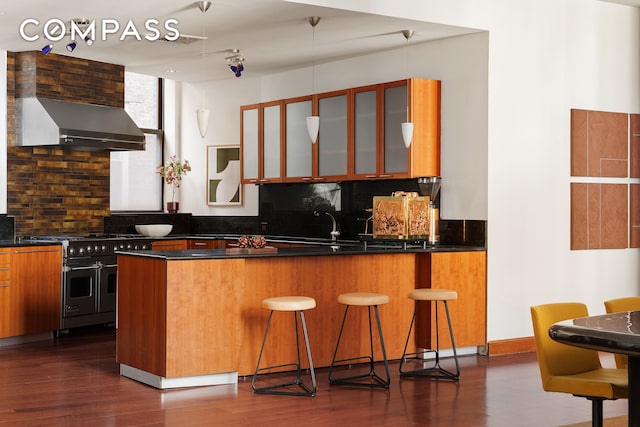 kitchen with dark countertops, decorative backsplash, double oven range, and wall chimney exhaust hood