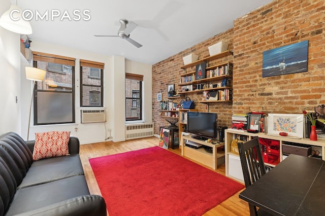 living room featuring radiator, ceiling fan, light wood-style flooring, and brick wall