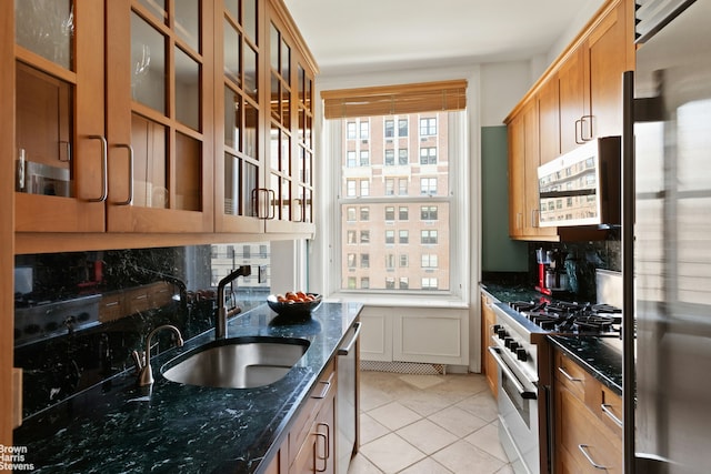 kitchen featuring backsplash, high quality appliances, a sink, light tile patterned floors, and dark stone countertops