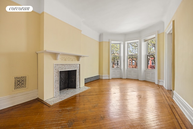 unfurnished living room featuring visible vents, baseboards, a high end fireplace, a baseboard heating unit, and hardwood / wood-style flooring