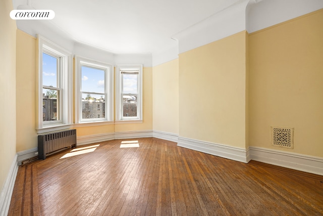 empty room featuring baseboards, visible vents, radiator heating unit, and hardwood / wood-style floors