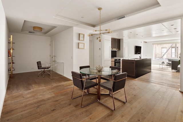 dining area featuring baseboards, a tray ceiling, light wood finished floors, and visible vents