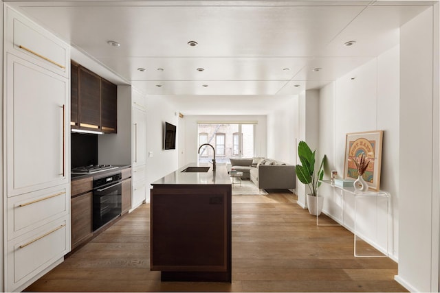 kitchen featuring a kitchen island with sink, stainless steel gas cooktop, a sink, open floor plan, and black oven