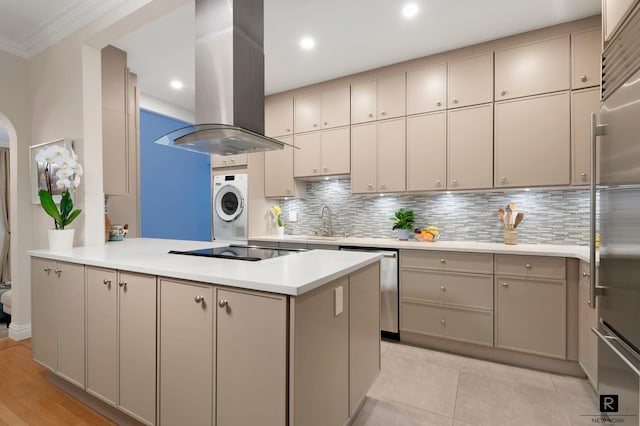 kitchen with appliances with stainless steel finishes, light countertops, a peninsula, island range hood, and backsplash
