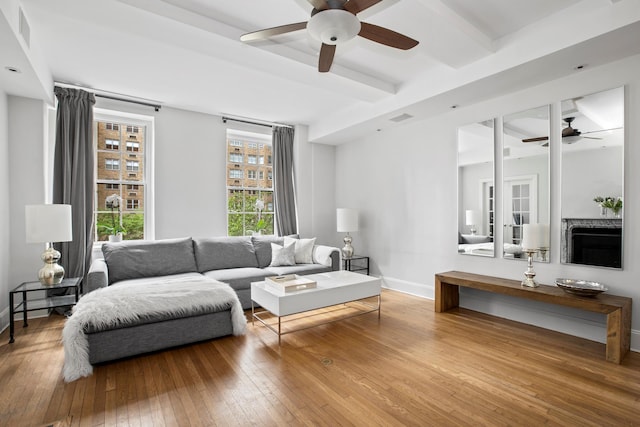 living area featuring ceiling fan, hardwood / wood-style floors, baseboards, beamed ceiling, and visible vents