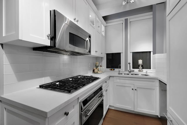 kitchen with appliances with stainless steel finishes, tasteful backsplash, a sink, light countertops, and white cabinetry
