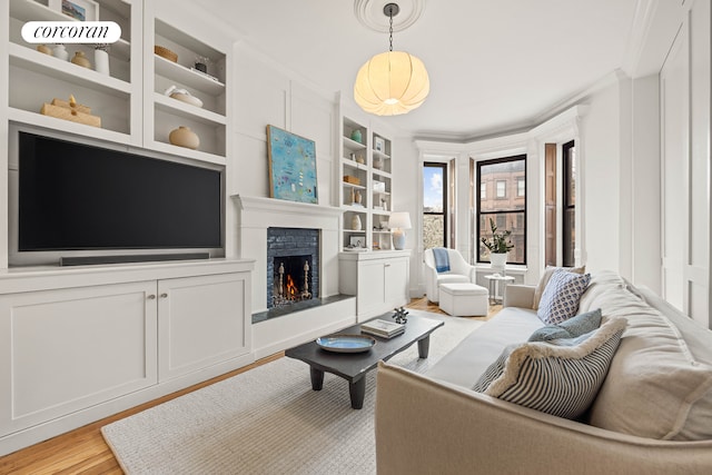 living area featuring crown molding, a warm lit fireplace, built in shelves, and light wood finished floors