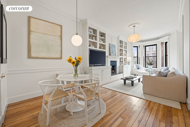 living area featuring crown molding, wood-type flooring, a warm lit fireplace, and built in shelves