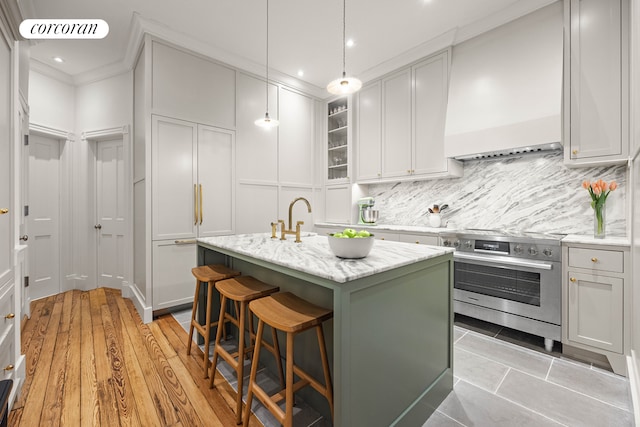 kitchen with a kitchen island with sink, oven, a kitchen breakfast bar, tasteful backsplash, and high end stove