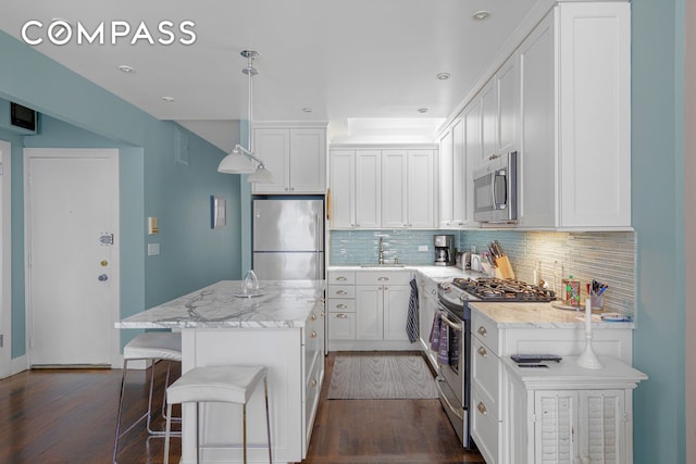 kitchen featuring dark wood-style flooring, a center island, white cabinets, appliances with stainless steel finishes, and backsplash