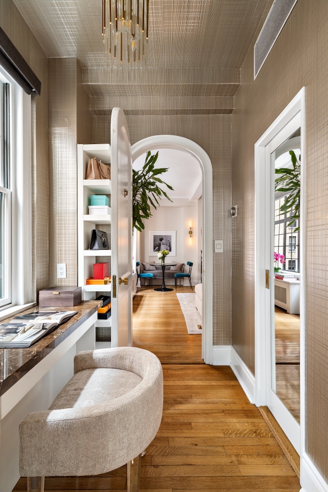hall featuring arched walkways, wood finished floors, and a chandelier