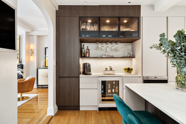 bar with oven, arched walkways, light wood-type flooring, indoor bar, and wine cooler