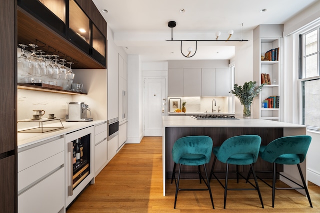 bar with a sink, stainless steel gas cooktop, light wood-type flooring, wine cooler, and bar area