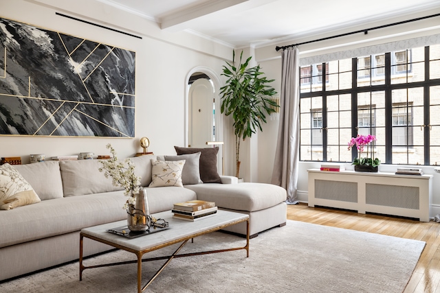 living area with ornamental molding, wood finished floors, beamed ceiling, radiator heating unit, and arched walkways