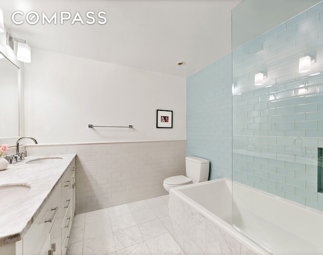 full bath with a sink, double vanity, toilet, a wainscoted wall, and tile walls