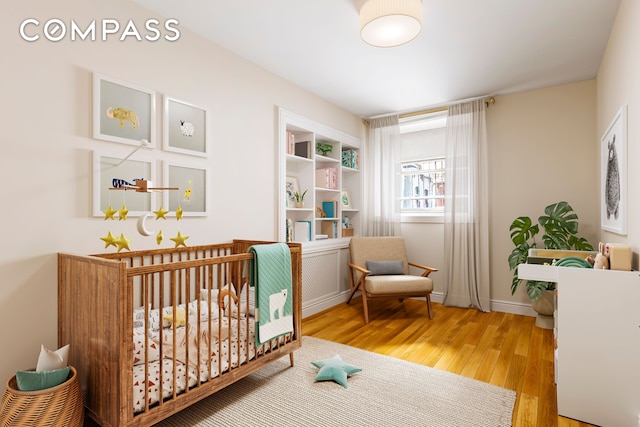bedroom featuring baseboards, wood finished floors, and a nursery area