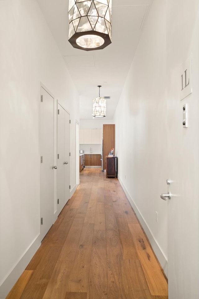 hallway featuring visible vents, light wood-style flooring, and baseboards