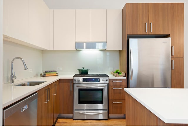 220 W 148th St Unit 1L, New York City, NY 10039 - kitchen with stainless steel appliances, a sink, under cabinet range hood, brown cabinetry, and light countertops