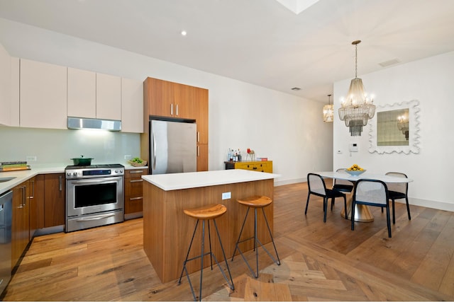 kitchen featuring a breakfast bar area, a center island, light countertops, ventilation hood, and stainless steel appliances