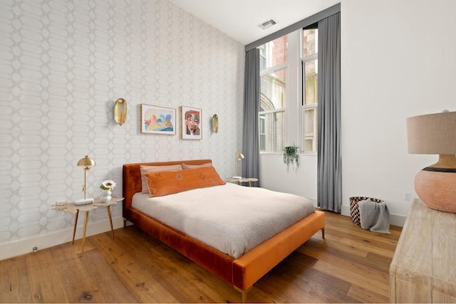 bedroom with baseboards, wallpapered walls, wood finished floors, and visible vents