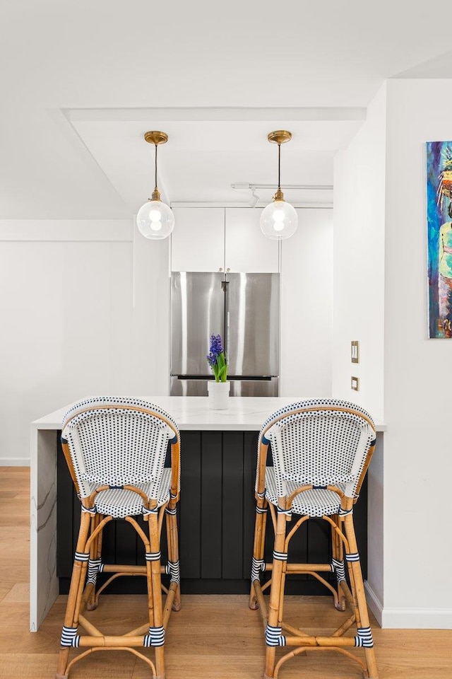 bar featuring baseboards, freestanding refrigerator, pendant lighting, and light wood-style flooring