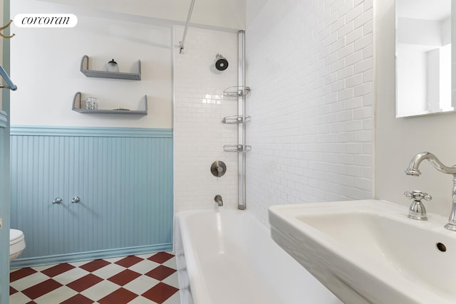 bathroom featuring wainscoting, a sink, tile patterned floors, toilet, and tub / shower combination