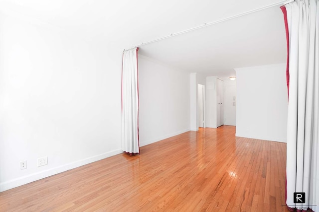 unfurnished room with crown molding, baseboards, and light wood-type flooring
