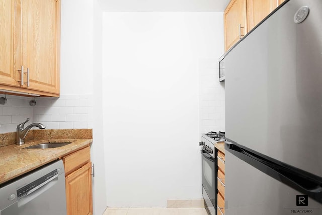 kitchen featuring range with gas stovetop, freestanding refrigerator, light brown cabinetry, dishwashing machine, and a sink
