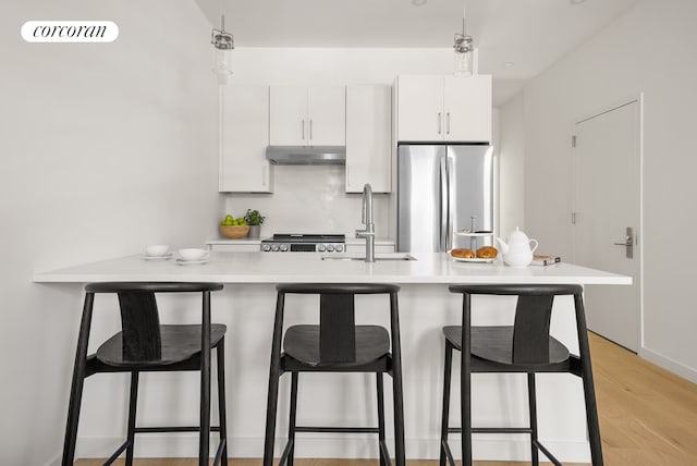 291 6th Ave Unit 4, New York City, NY 11215 - kitchen featuring under cabinet range hood, stainless steel appliances, light countertops, a breakfast bar, and pendant lighting