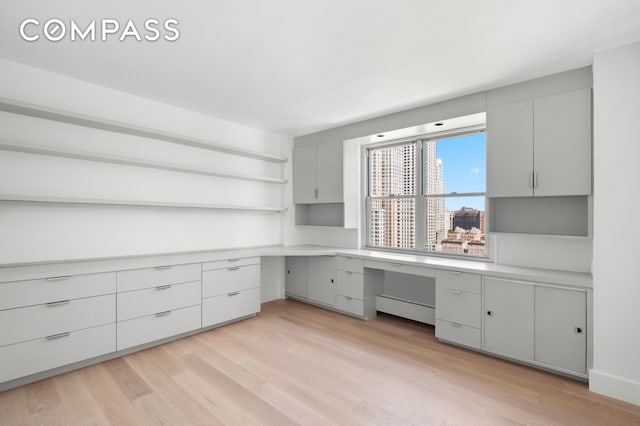 unfurnished office with a view of city, built in desk, and light wood-type flooring
