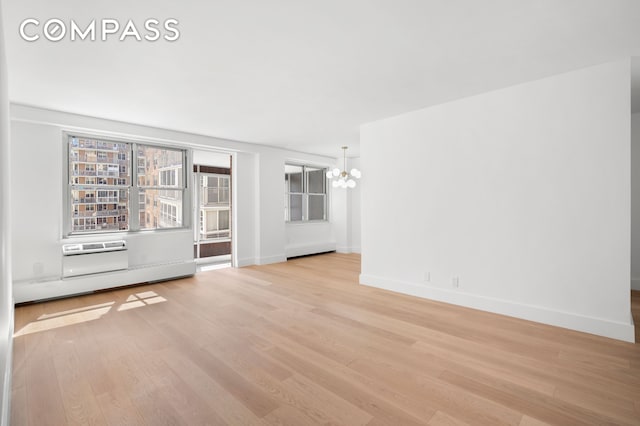 unfurnished living room with baseboards, an inviting chandelier, and light wood-style floors