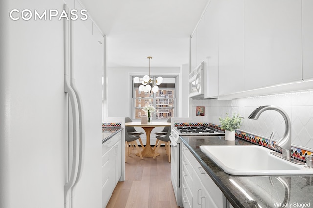 kitchen with dark countertops, a sink, white appliances, white cabinetry, and decorative backsplash
