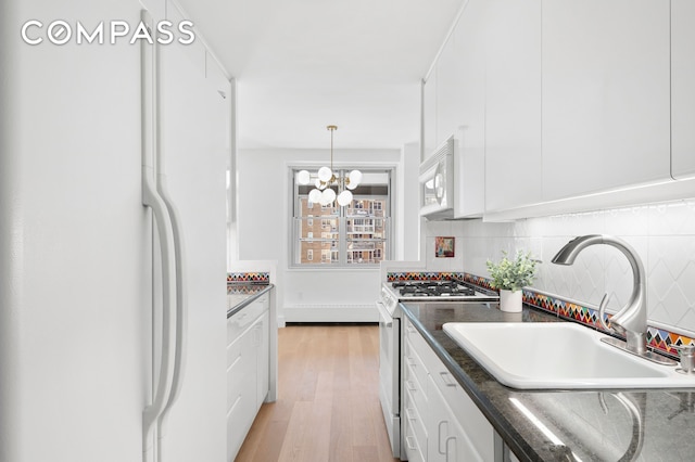 kitchen with dark countertops, white appliances, white cabinets, a sink, and backsplash