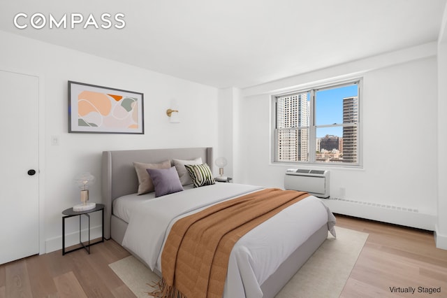 bedroom with light wood-type flooring, a wall mounted air conditioner, and a baseboard radiator