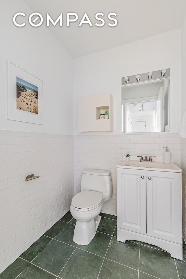bathroom with vanity, tile patterned flooring, wainscoting, toilet, and tile walls