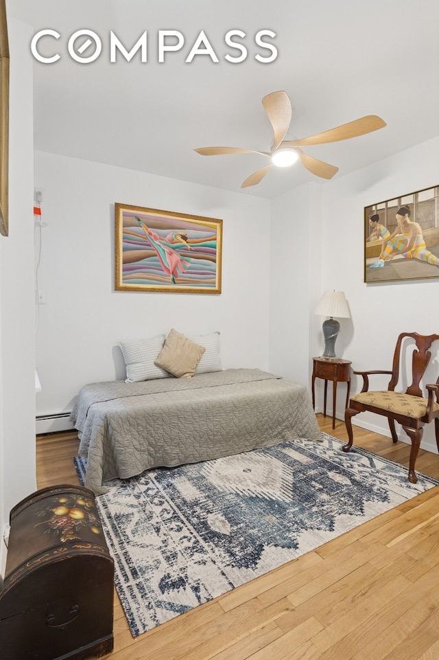 bedroom featuring a baseboard heating unit, wood finished floors, and a ceiling fan