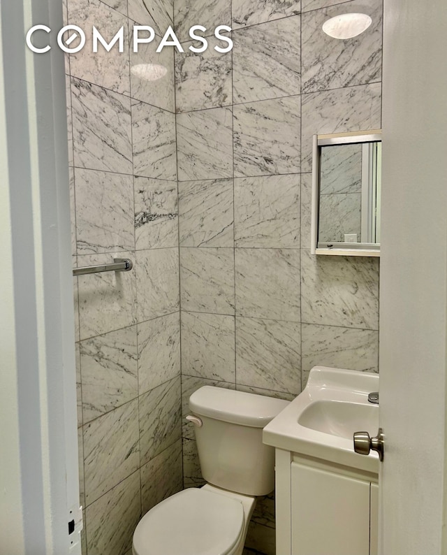 bathroom featuring vanity, toilet, and tile walls