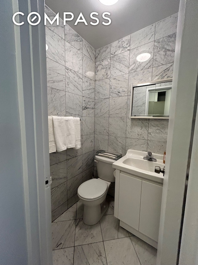 400 E 54th St Unit 15E, New York City, NY 10022 - half bathroom with vanity, toilet, marble look tiles, and tile walls