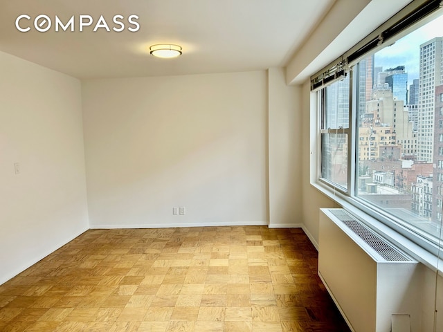 empty room with baseboards, radiator heating unit, and a city view