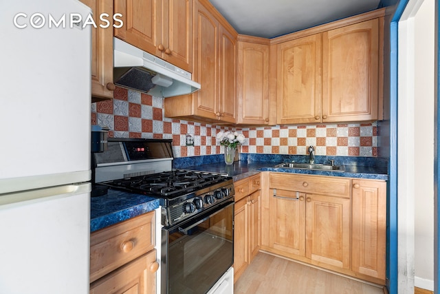 kitchen with freestanding refrigerator, dark countertops, under cabinet range hood, a sink, and black range with gas cooktop