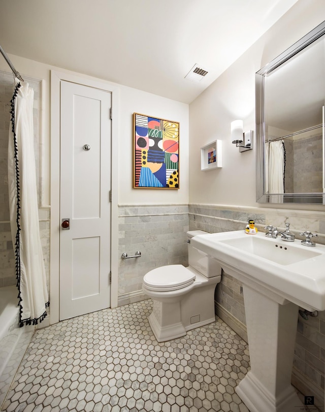 full bath featuring tile patterned flooring, toilet, tile walls, a shower with shower curtain, and a wainscoted wall