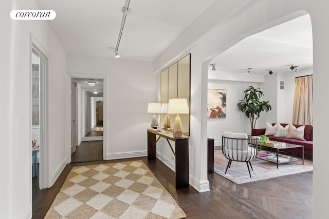 corridor featuring baseboards, rail lighting, wood finished floors, and visible vents