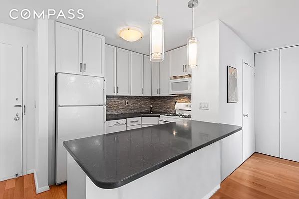 kitchen featuring white cabinets, dark countertops, white appliances, light wood-style flooring, and backsplash