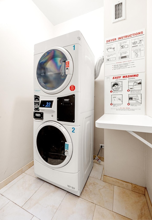 laundry room with baseboards, laundry area, stacked washing maching and dryer, and light tile patterned floors