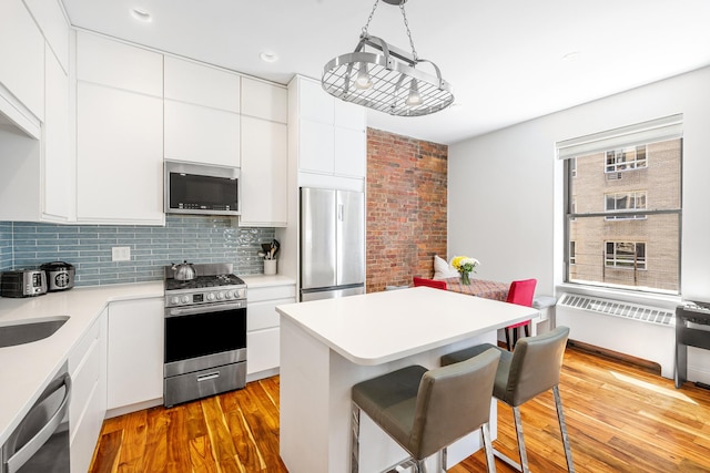 kitchen with decorative backsplash, wood finished floors, a breakfast bar area, white cabinets, and appliances with stainless steel finishes