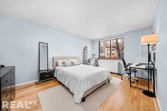 bedroom featuring baseboards, light wood-style flooring, and radiator
